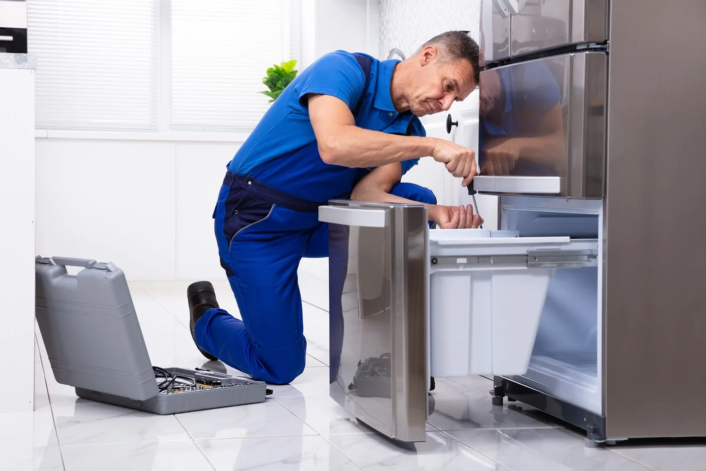 Service technician repairing a refrigerator in a bright residential kitchen