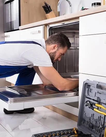 Technician inspecting the interior of a dishwasher with a repair tool kit nearby