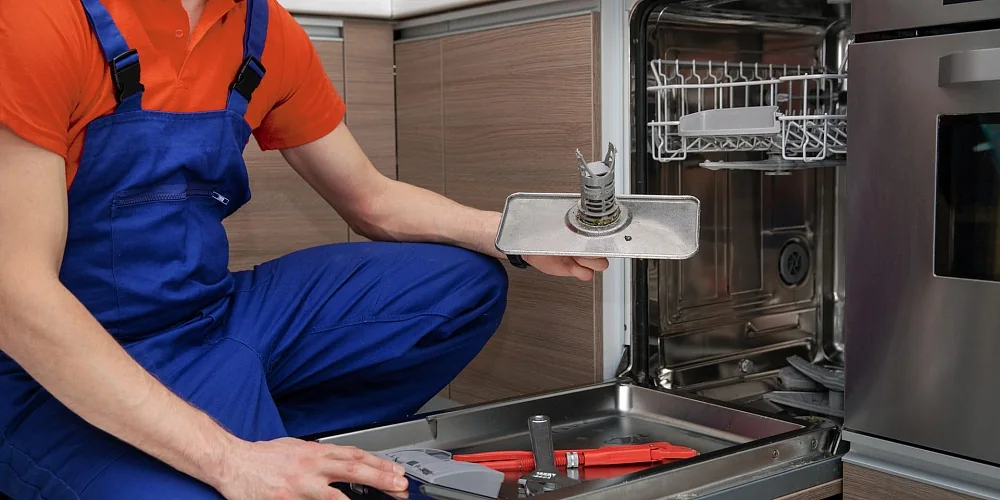 Appliance repair technician servicing an open dishwasher in a residential kitchen