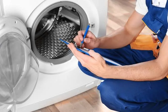 Appliance technician documenting an inspection beside a front-loading laundry machine