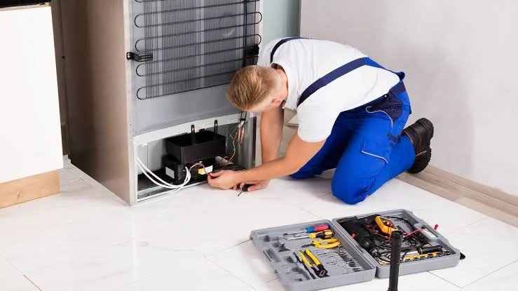 Technician testing components behind a household refrigerator