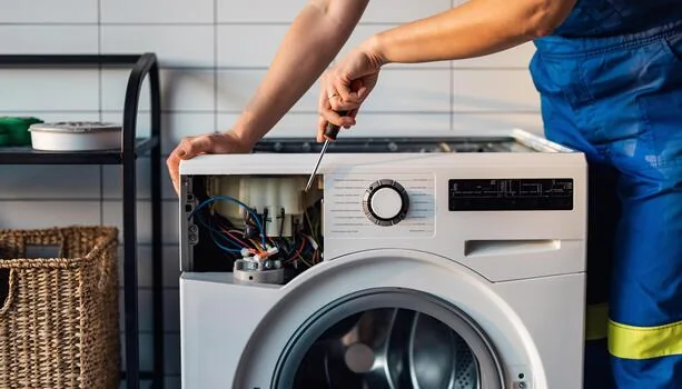 Technician using a screwdriver to inspect washing machine controls
